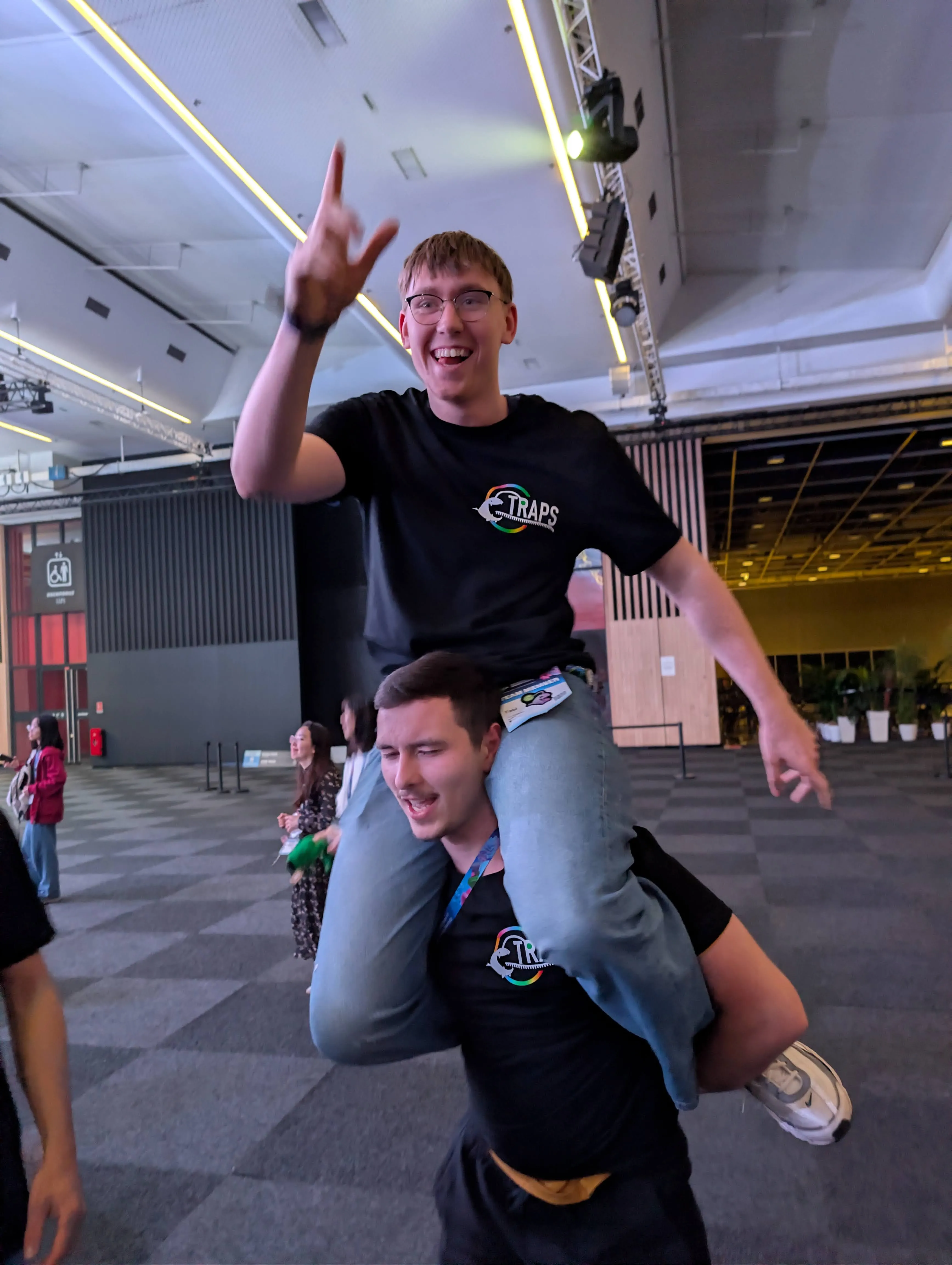 A young man sitting on the shoulders of another, they are celebrating.