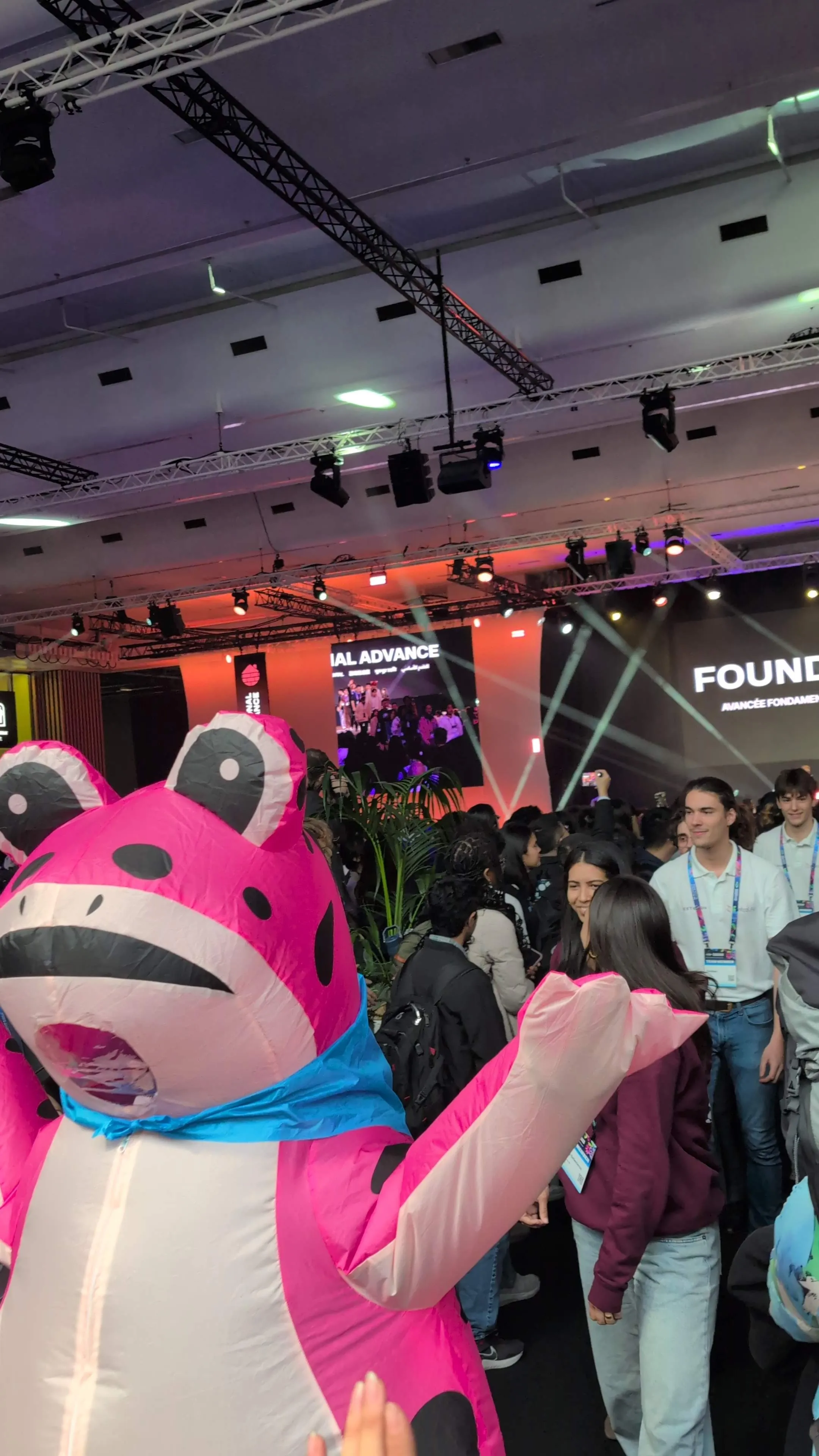 A person in a pink frog costume is walking in front of the Grand Jamboree stage.