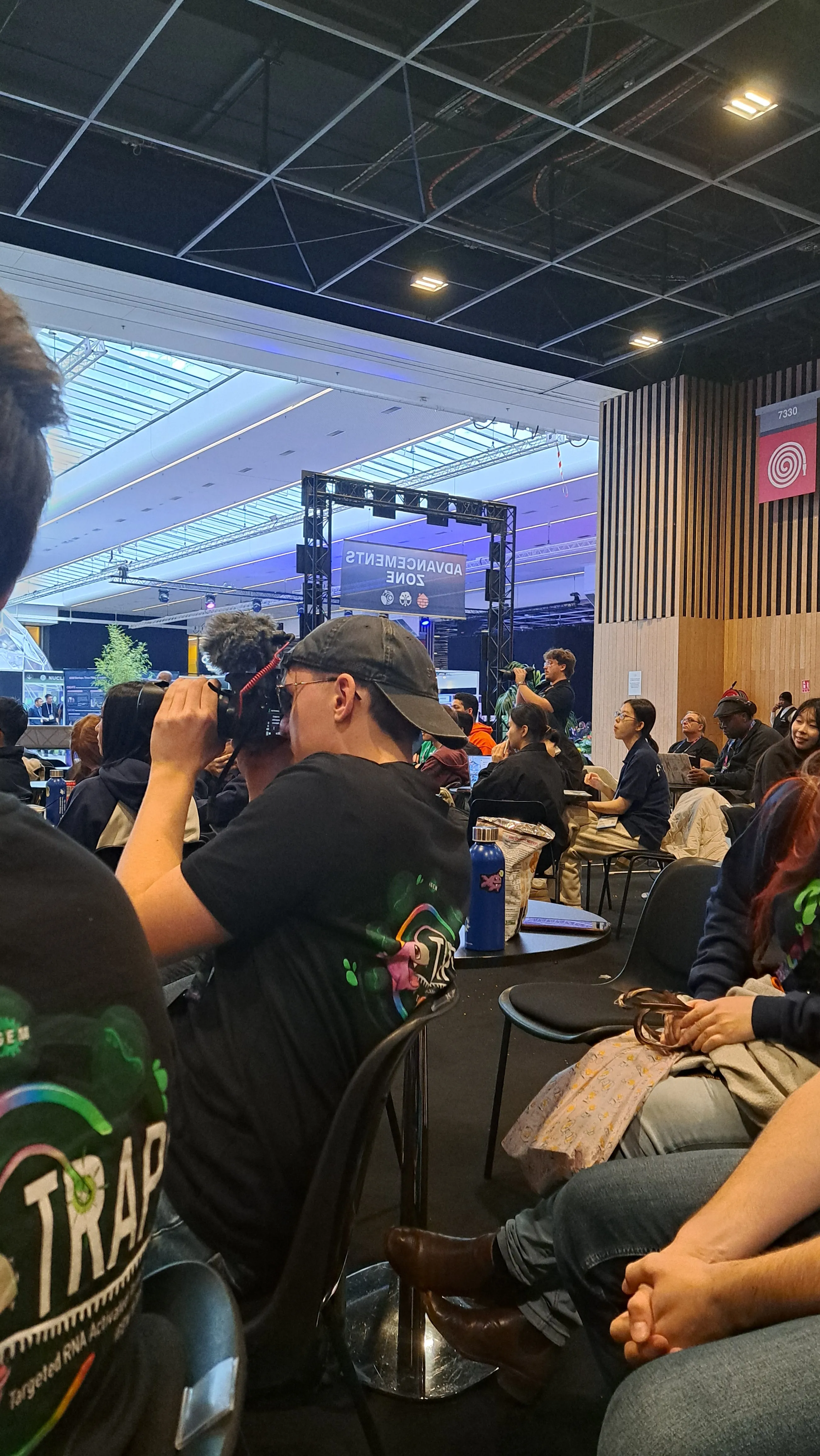 Two members of the team are taking pictures of their team members presenting on stage with big cameras