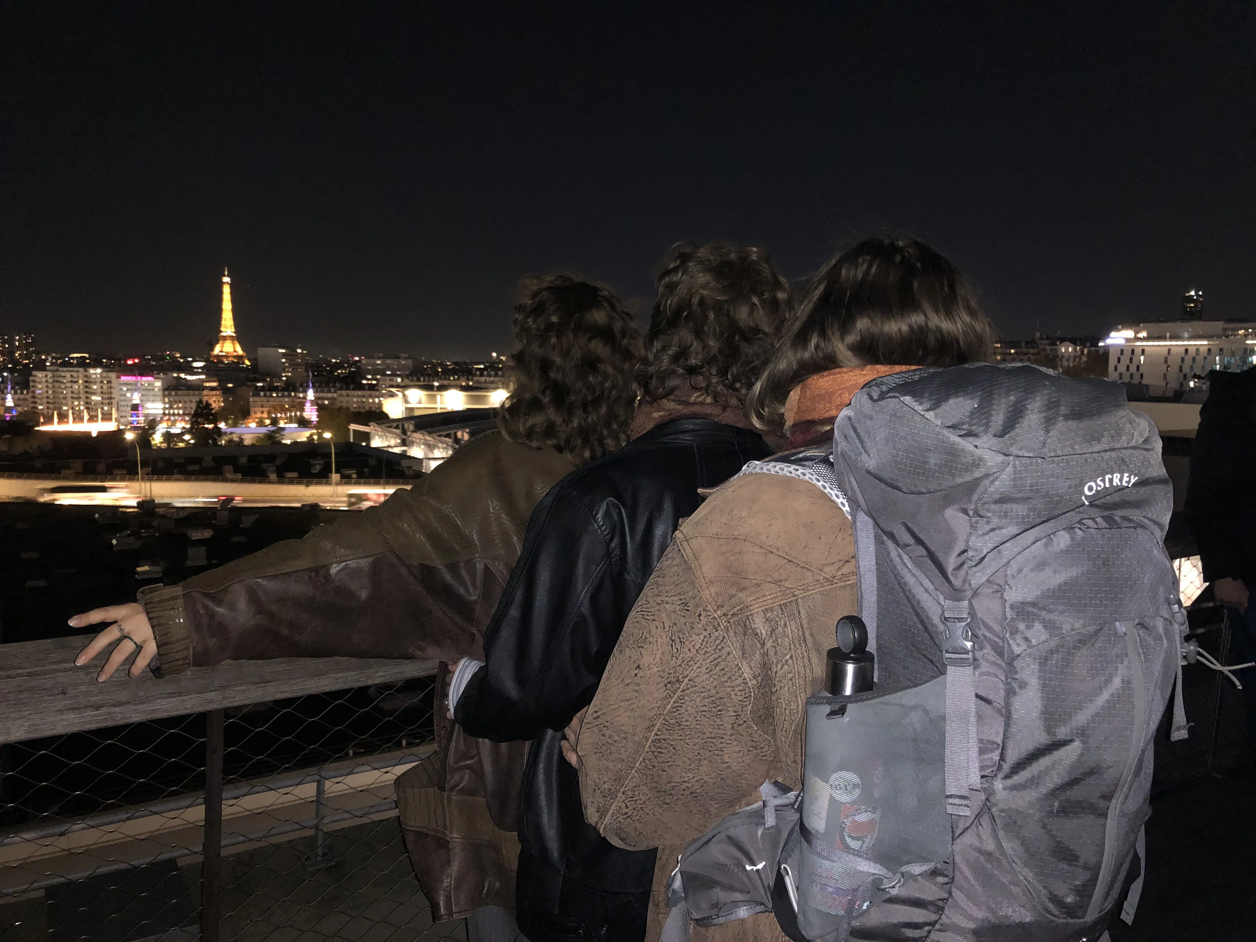 The view on the Eiffel tower from a rooftop. Three members of the team are posing in front of it.
