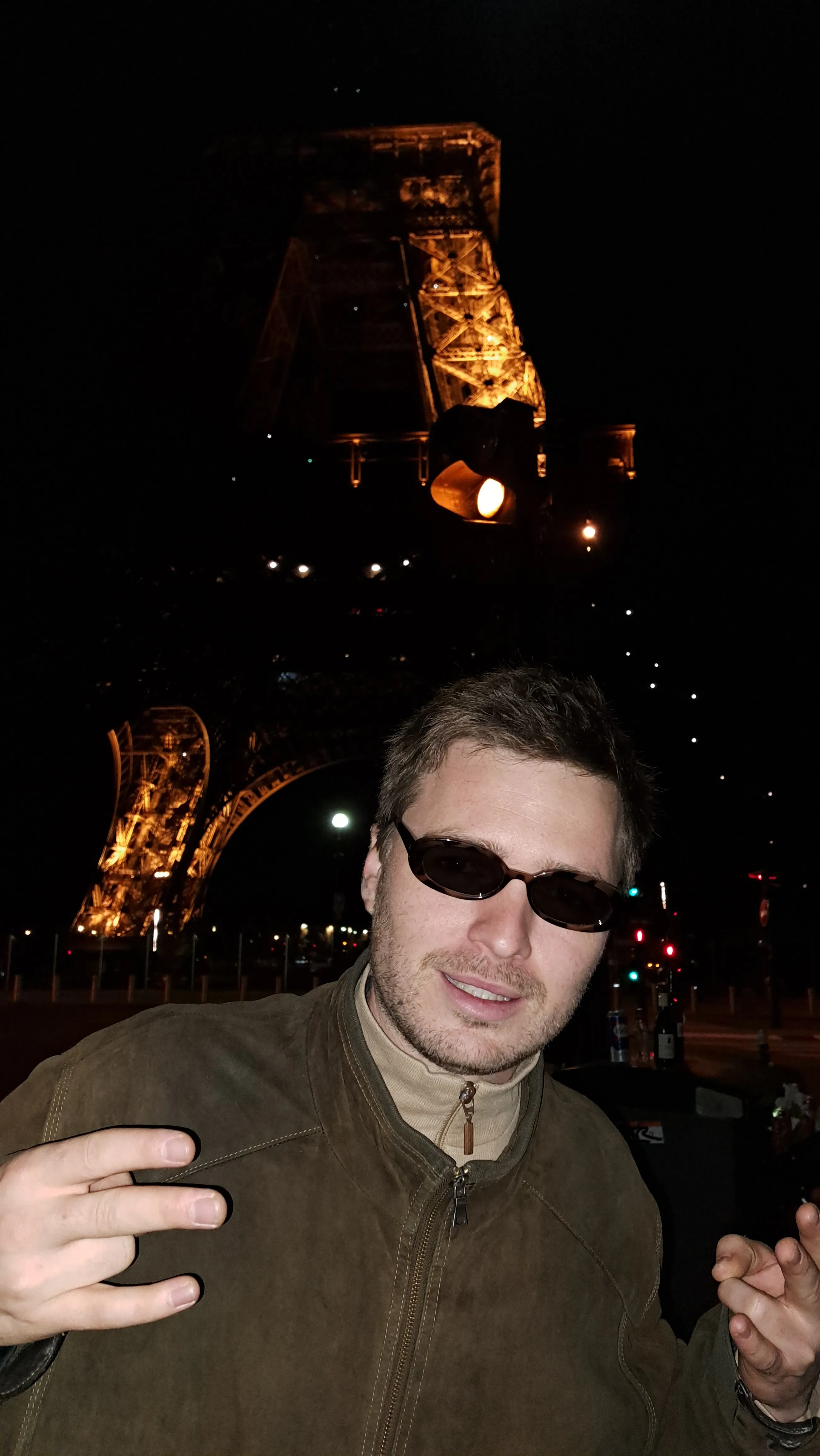 A guy with sunglasses posing in front of the Eiffel tower.