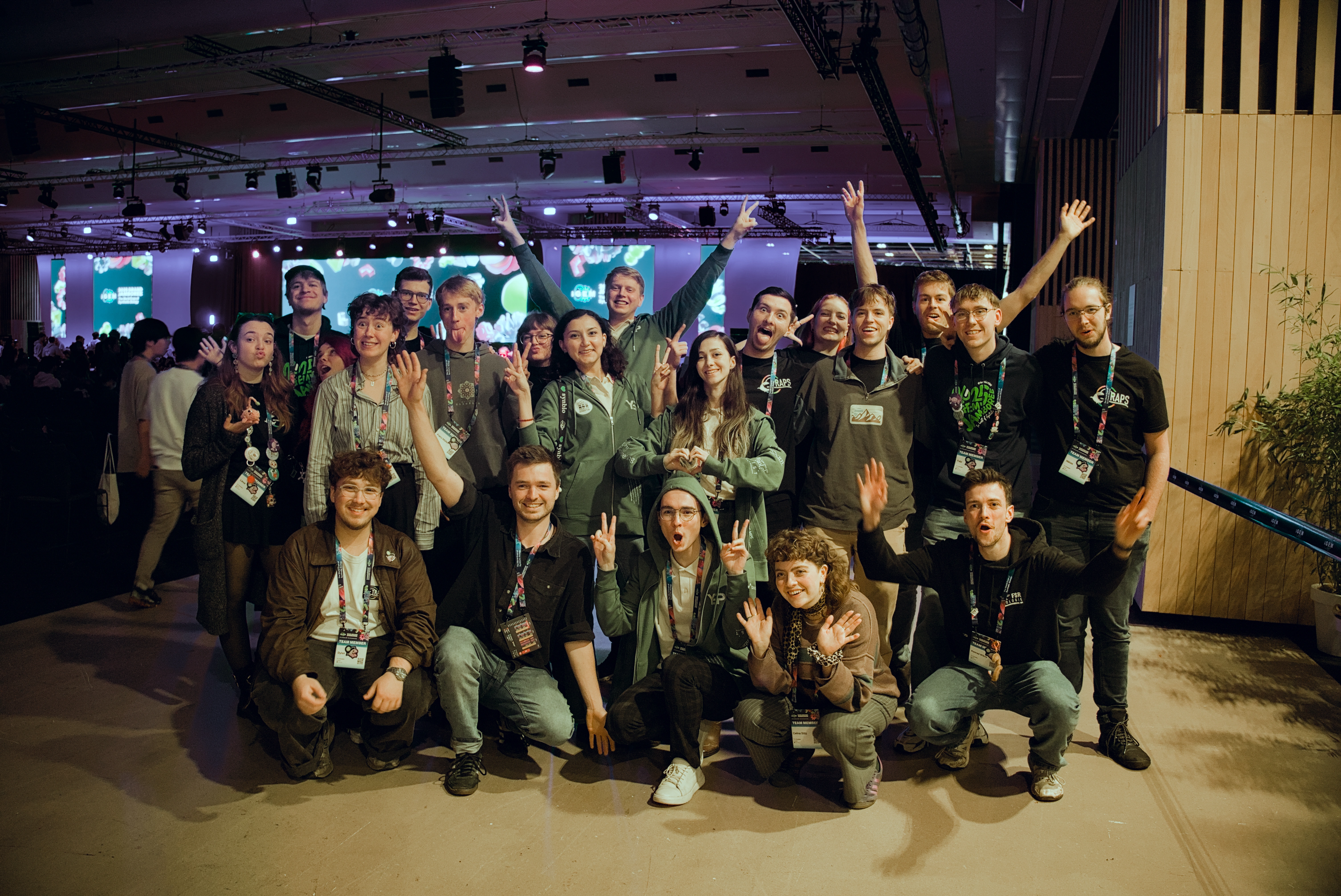 Two iGEM teams posing together in front of the Grand Jamboree stage.