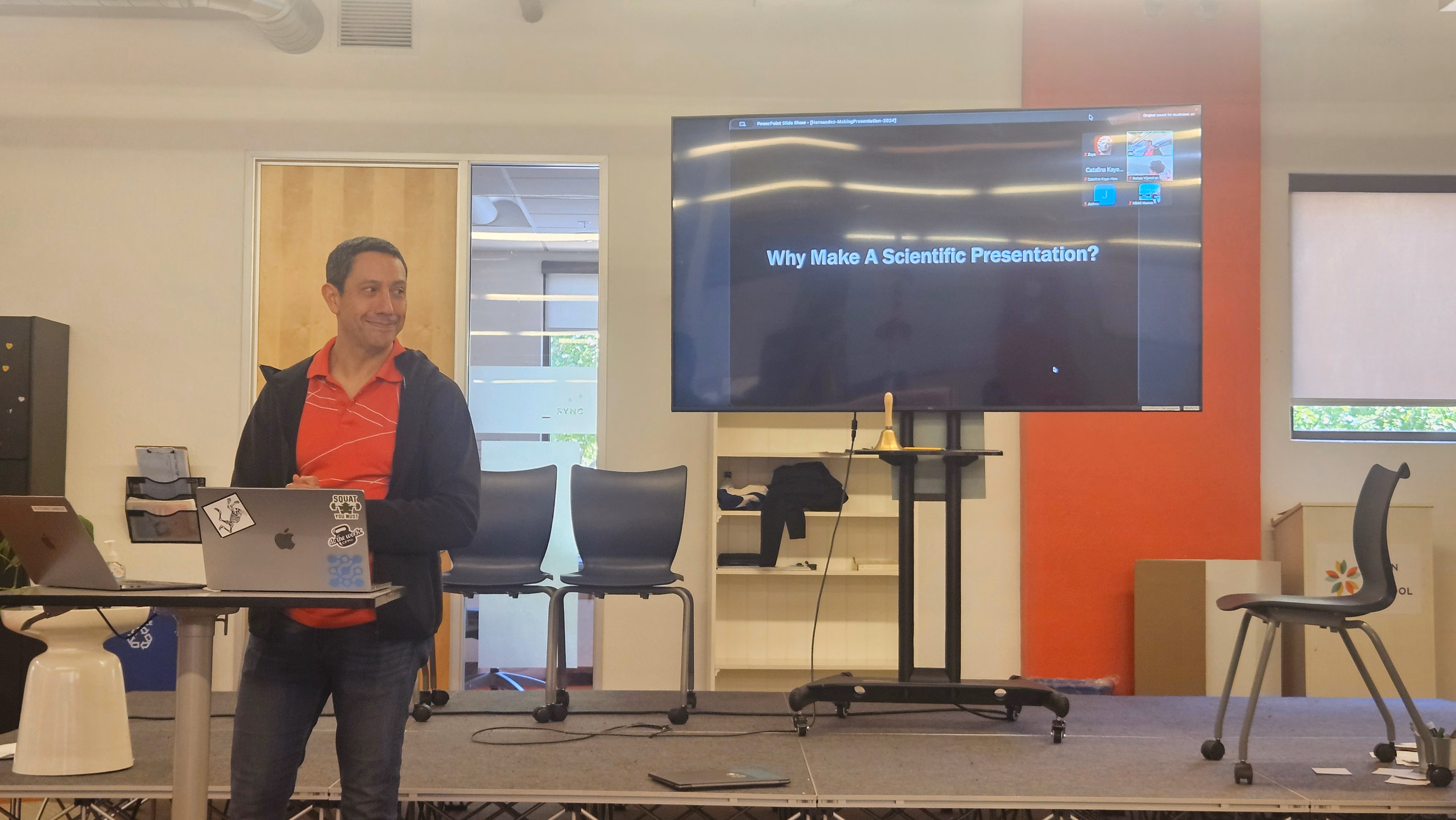 Christopher Hernandez standing in front of a TV with a slide labeled why make a scientific presentation.