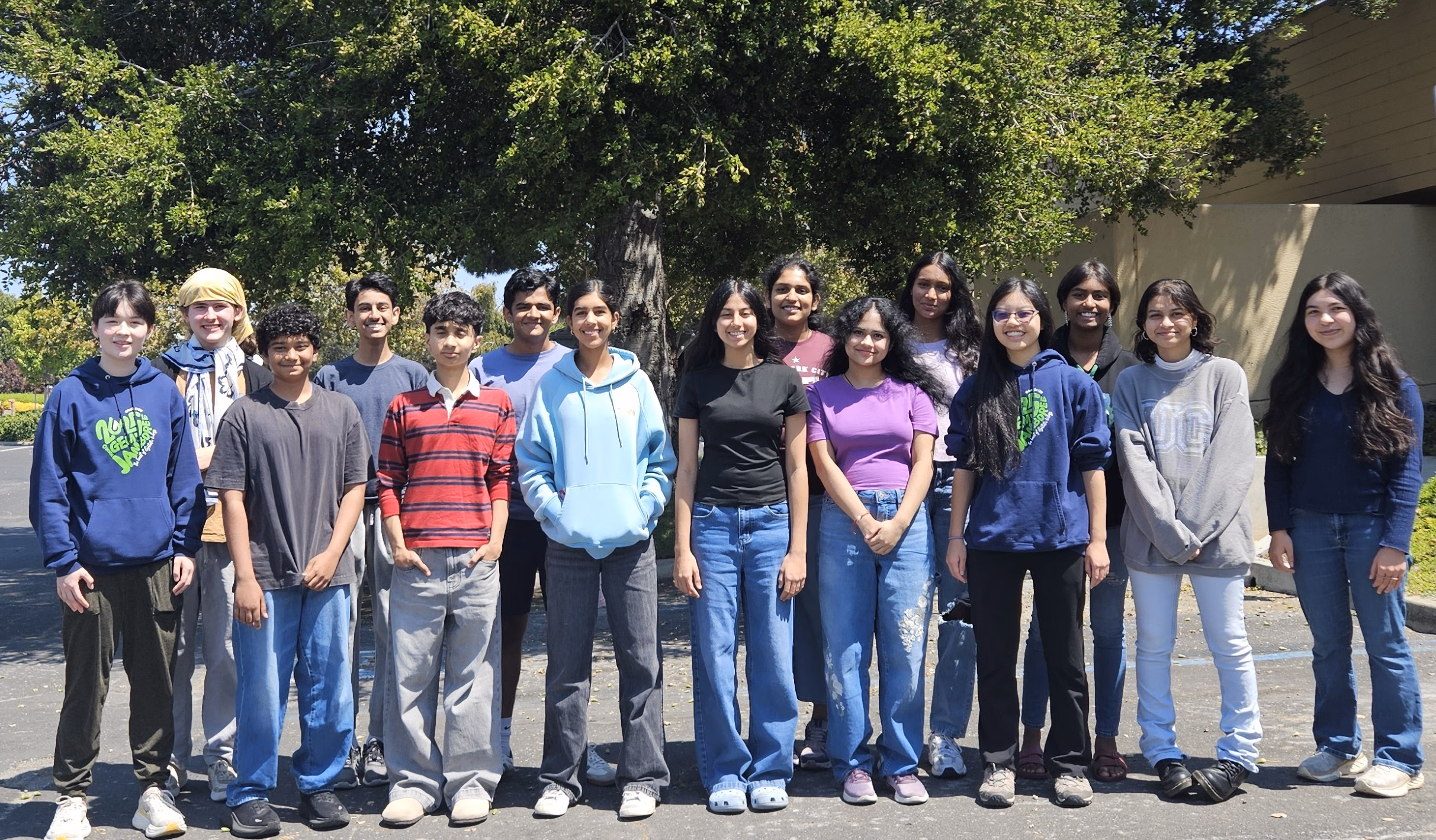 15 team members standing next to each other in front of a tree.