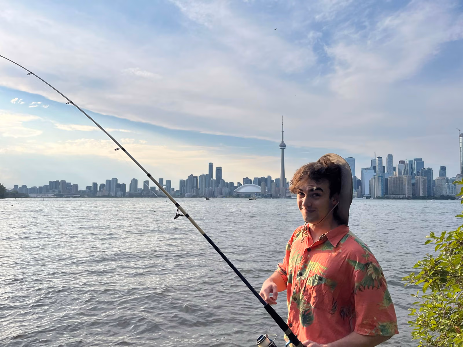 A team member in a red shirt fishing off Centre Island with the Toronto skyline behind
