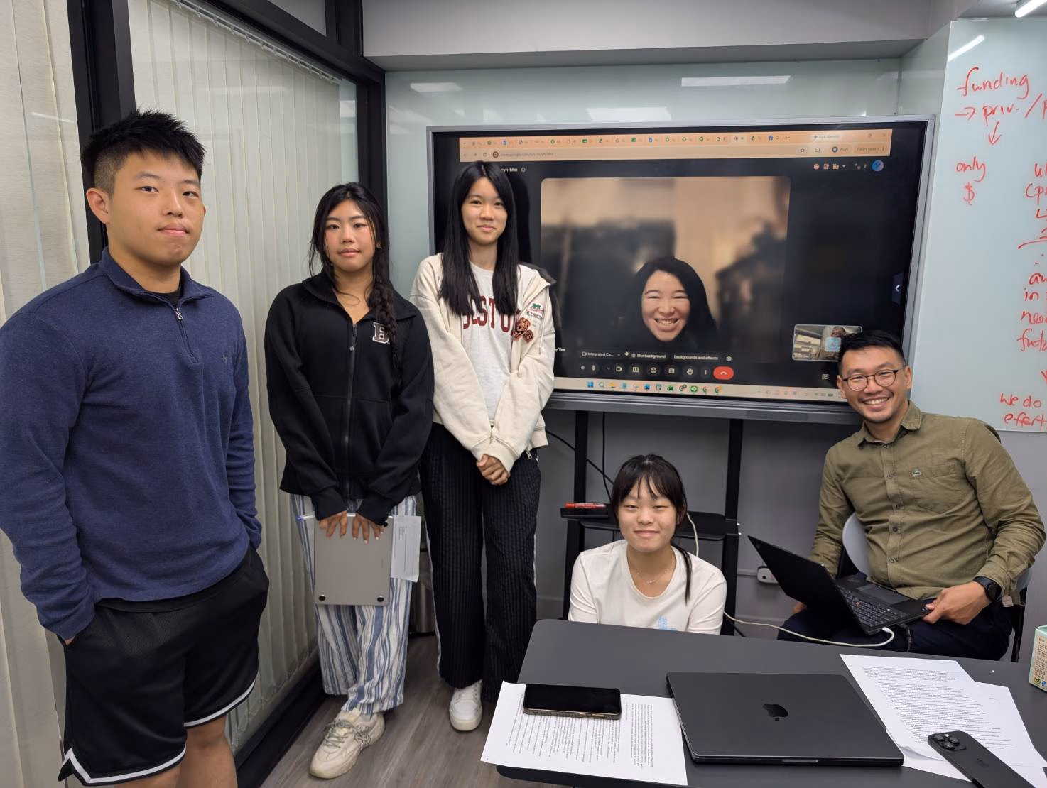 Team members interviewing Lindsey via video call, with the team gathered around a table and laptops